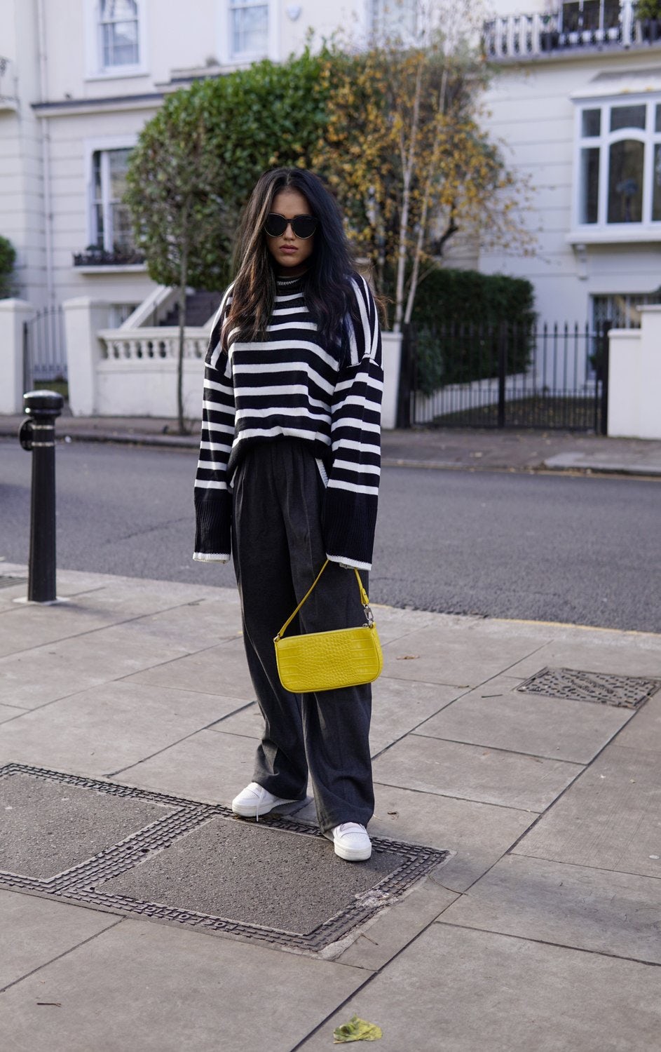 Sachini standing on a sidewalk wearing an oversized Chicwish striped jumper and trousers with a yellow bag